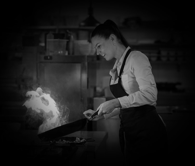A black and white photo of a woman cooking in a kitchen. Hospitality health and safety.